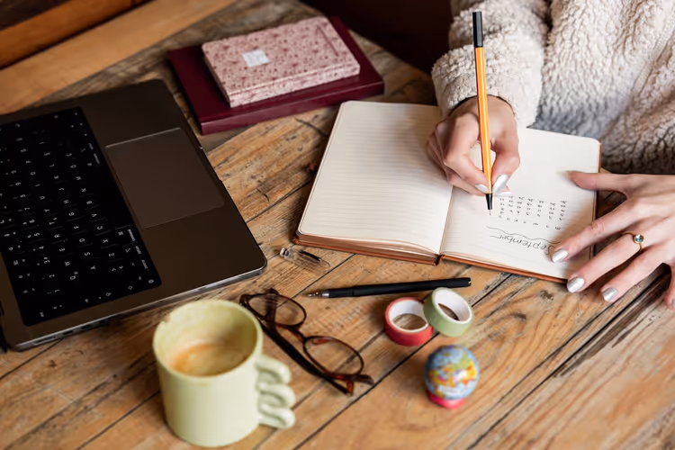Rédacteur corrigeant un manuscrit dans un carnet à côté d'un ordinateur portable avant de soumettre un article invité