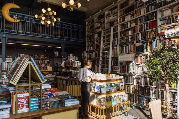 A reader flips through a book in a bright bookstore with tall shelves