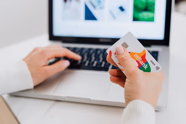 Customer's hands with a bank card at a laptop during checkout