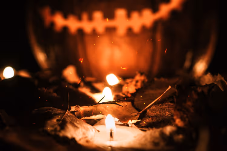 Pumpkin lantern with candles among fallen leaves at night