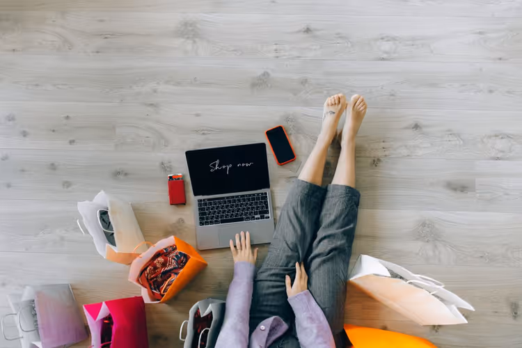 Shopper choosing products on a laptop surrounded by paper bags