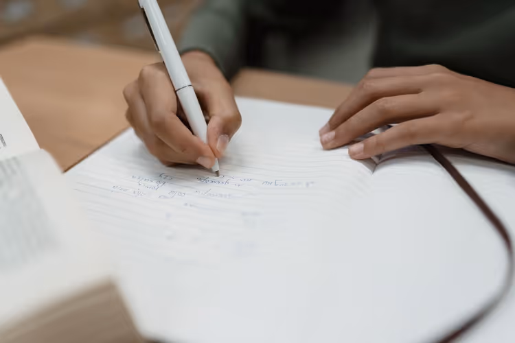 Close-up of a hand writing in an open notebook