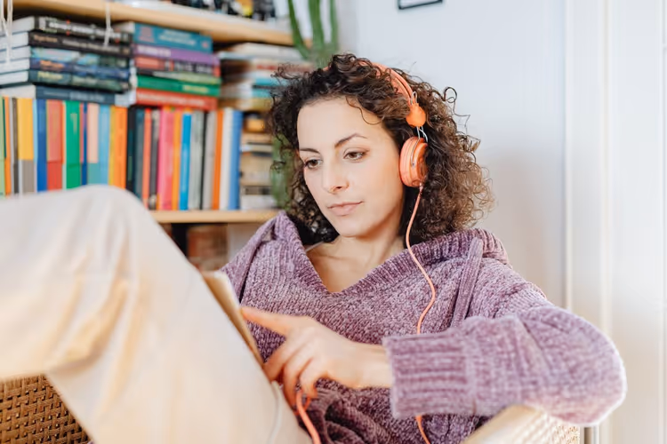 A female reader with a book and headphones combines reading and listening