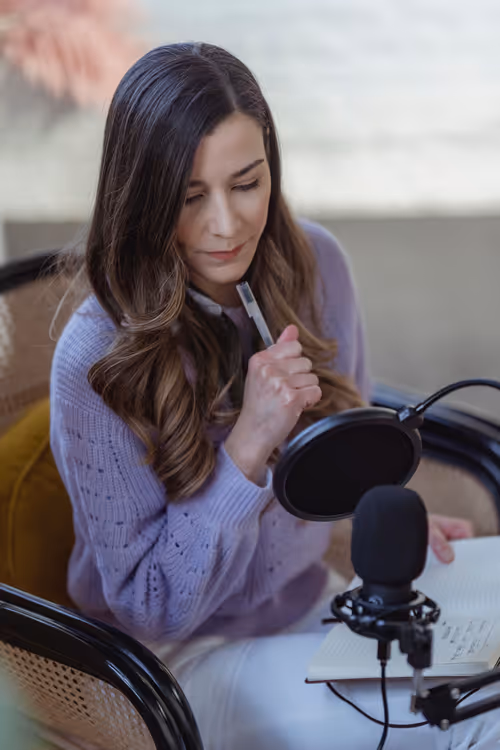 Kobieta z notatnikiem nagrywa podcast na mikrofon
