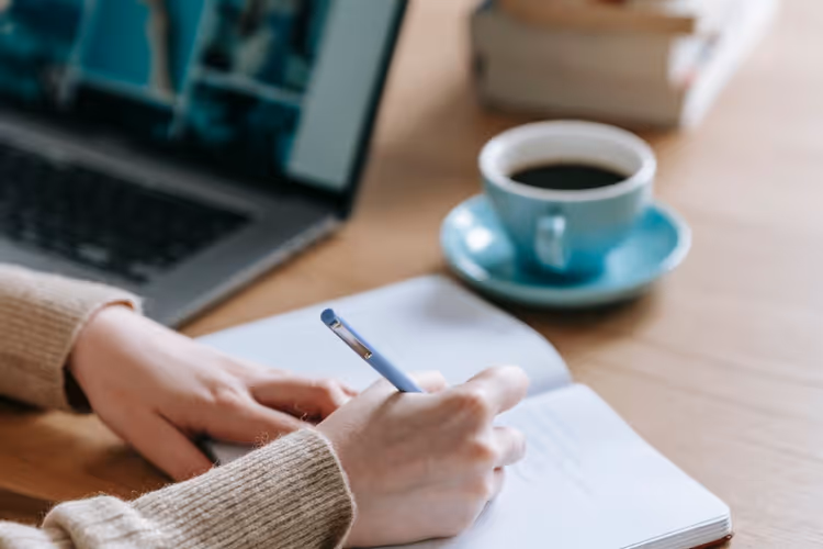 Writer jotting down an article plan in a notebook next to a laptop
